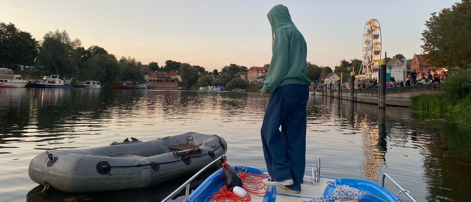Tretboot Schneewittchen neben dem Schlauchboot der Wassertombola im Havelberger Hafen, Festmeile und Riesenrad im Abendlicht