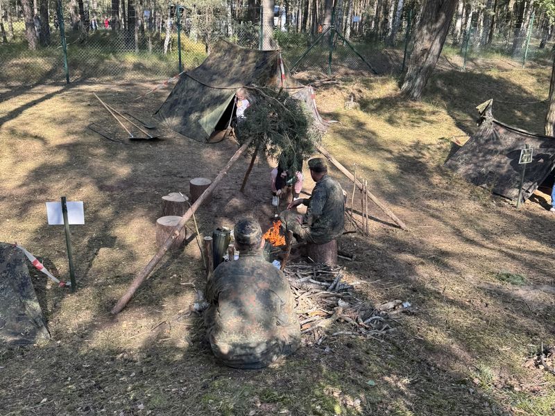 Soldiers and children at a campfire in front of tents in the pine wood at the Havelbiwak