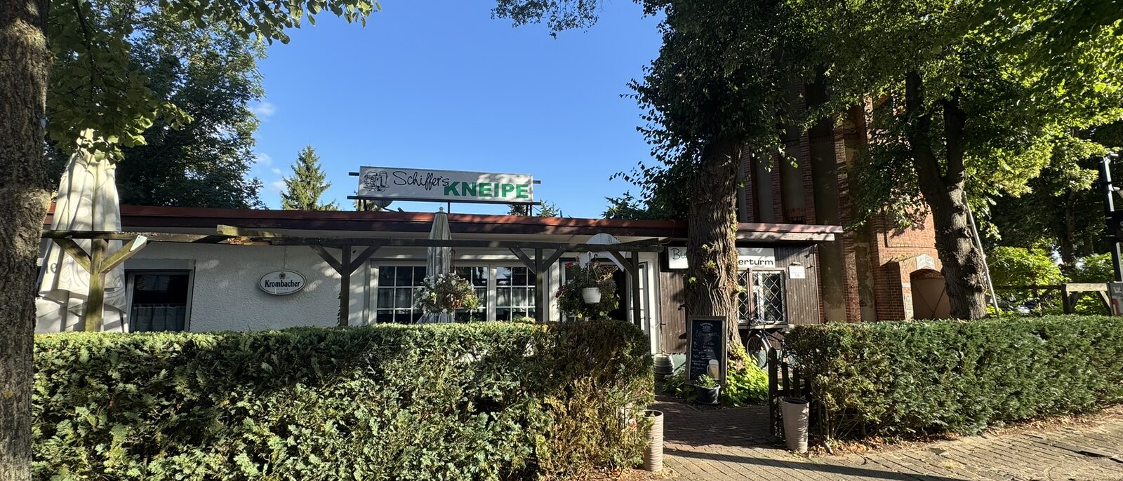 Schiffer's Kneipe in Havelberg, Eingang mit Schild und Hecke, im Hintergrund der Wasserturm